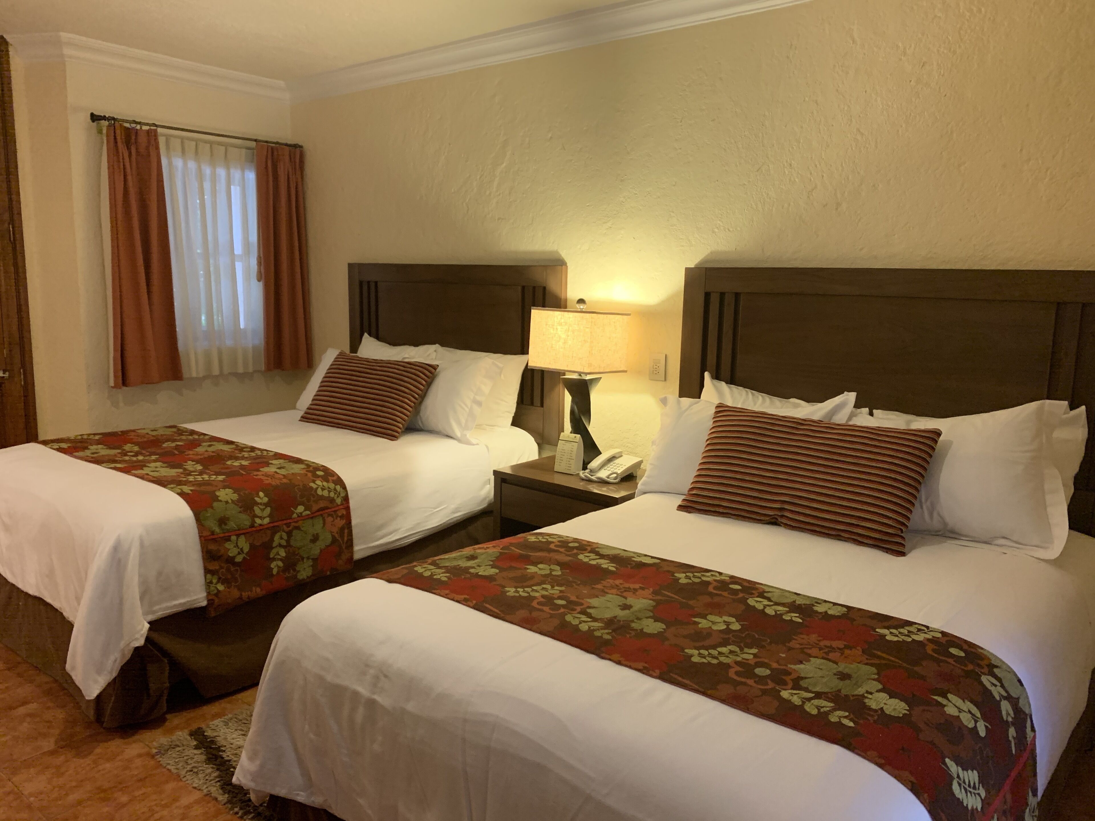 A hotel room with two beds, each with a floral bedspread, a nightstand with a lamp, and a telephone.