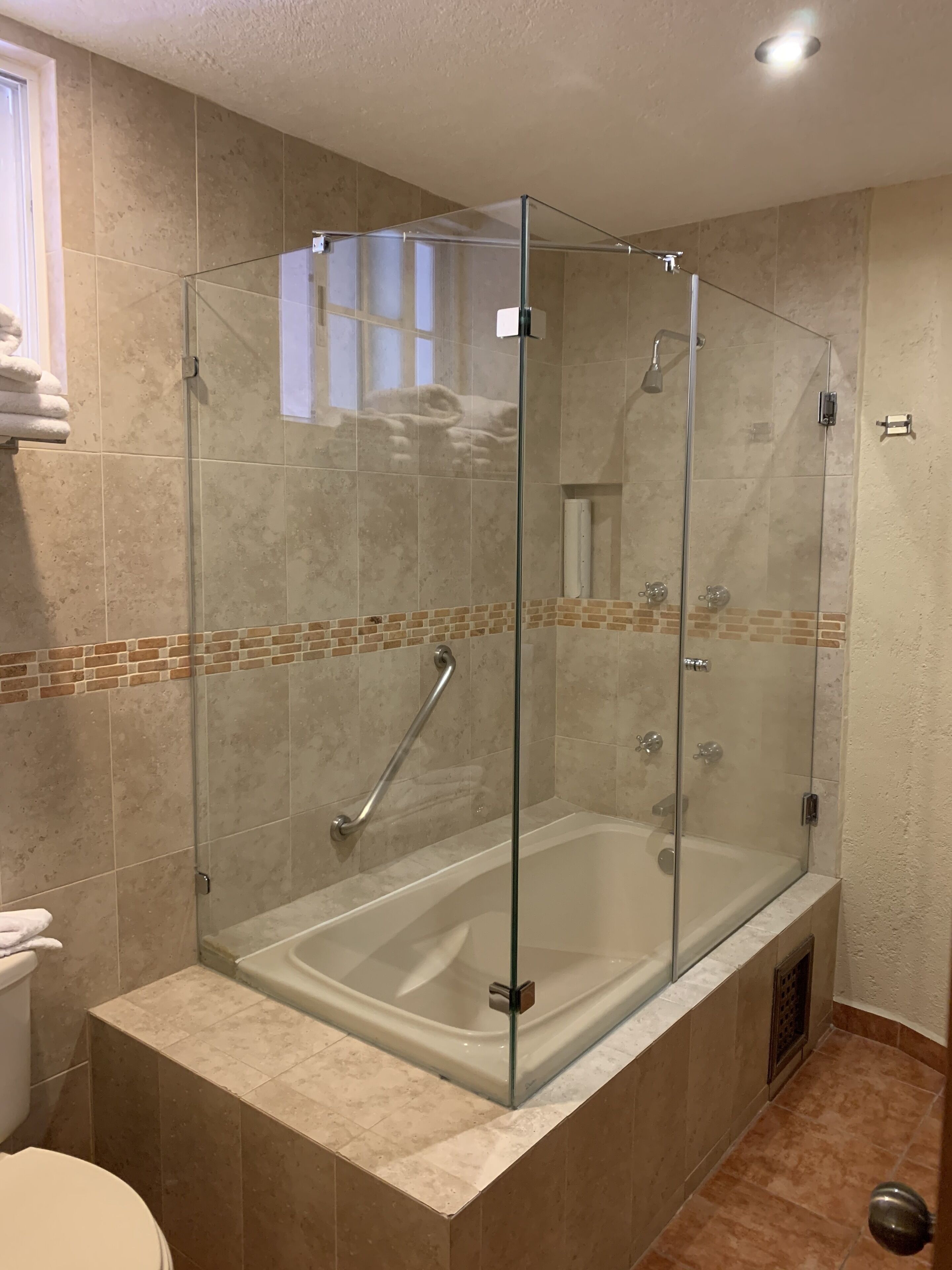 A glass-enclosed walk-in shower with a bathtub, beige tiles, and a small window.