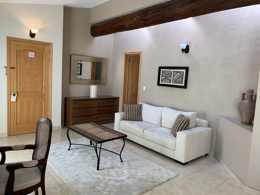 Una sala de estar con un sofá, una mesa de centro de madera, una silla, un aparador y un espejo.