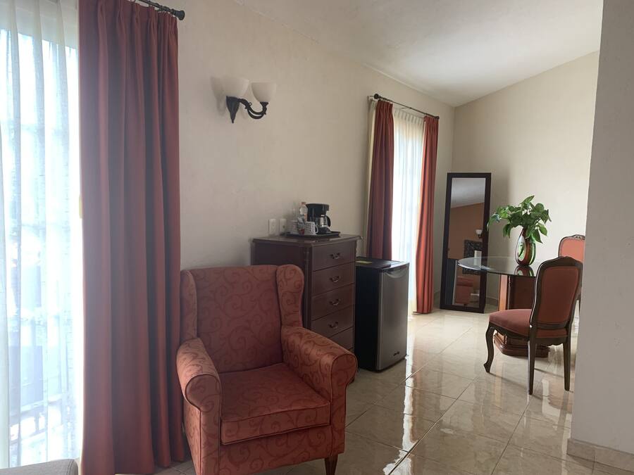 Ein Hotelzimmer mit Sofa, einer Kaffeemaschine, einem Kühlschrank, einem Esstisch mit Stühlen und einer Zimmerpflanze.
