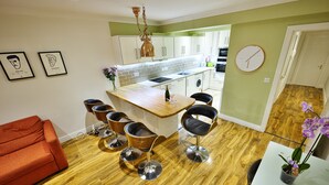 Une cuisine moderne avec un plan de travail en bois, des tabourets de bar, un canapé rouge et une table à manger agrémentée d’une orchidée en pot.