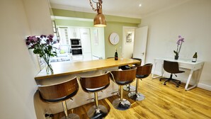Une cuisine moderne avec un îlot central en bois, des tabourets de bar et un coin repas comprenant une table et des chaises blanches.