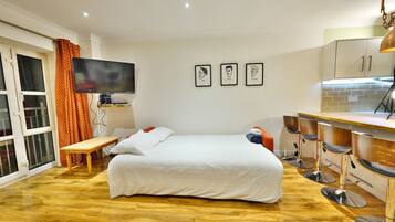 Habitación de hotel con cama, televisión, banca, escritorio y kitchenette con taburetes de bar.