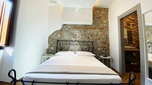 Un dormitorio con pared de piedra, una cama con ropa de cama blanca y una mesita de noche pequeña.