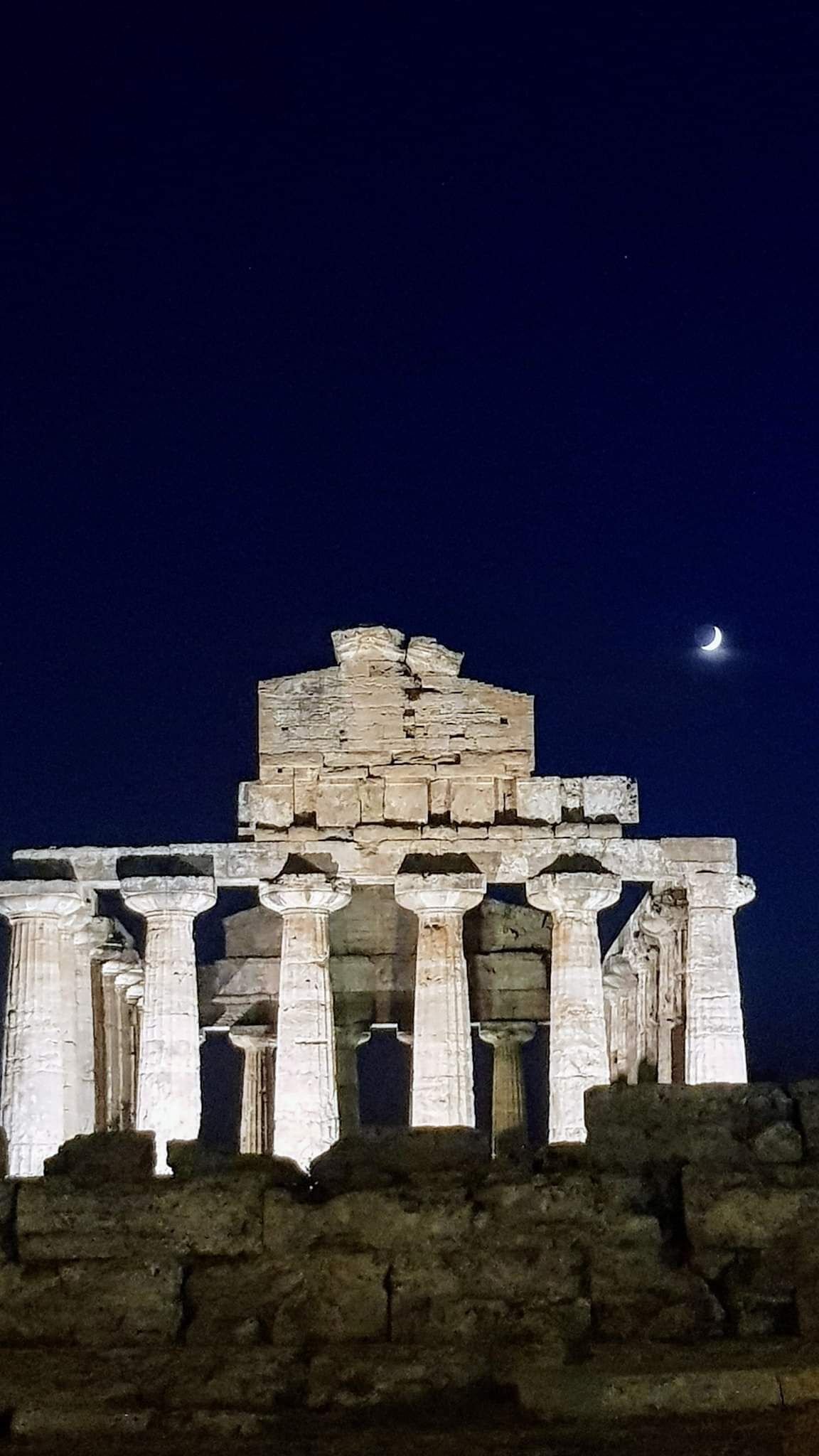 A historical structure with multiple columns and a central elevated platform, illuminated at night.