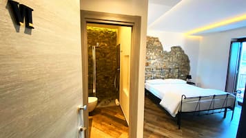 Ein modernes Schlafzimmer mit Holzboden, einem Bett mit Metallgestell, einer Steinwand und einem Badezimmer mit Duschkabine aus Stein.
