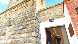 Un edificio de piedra con una torre, una entrada moderna y un cielo despejado.