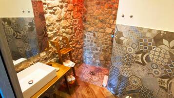 A bathroom with a stone wall, a wooden vanity, a toilet, and a shower area.
