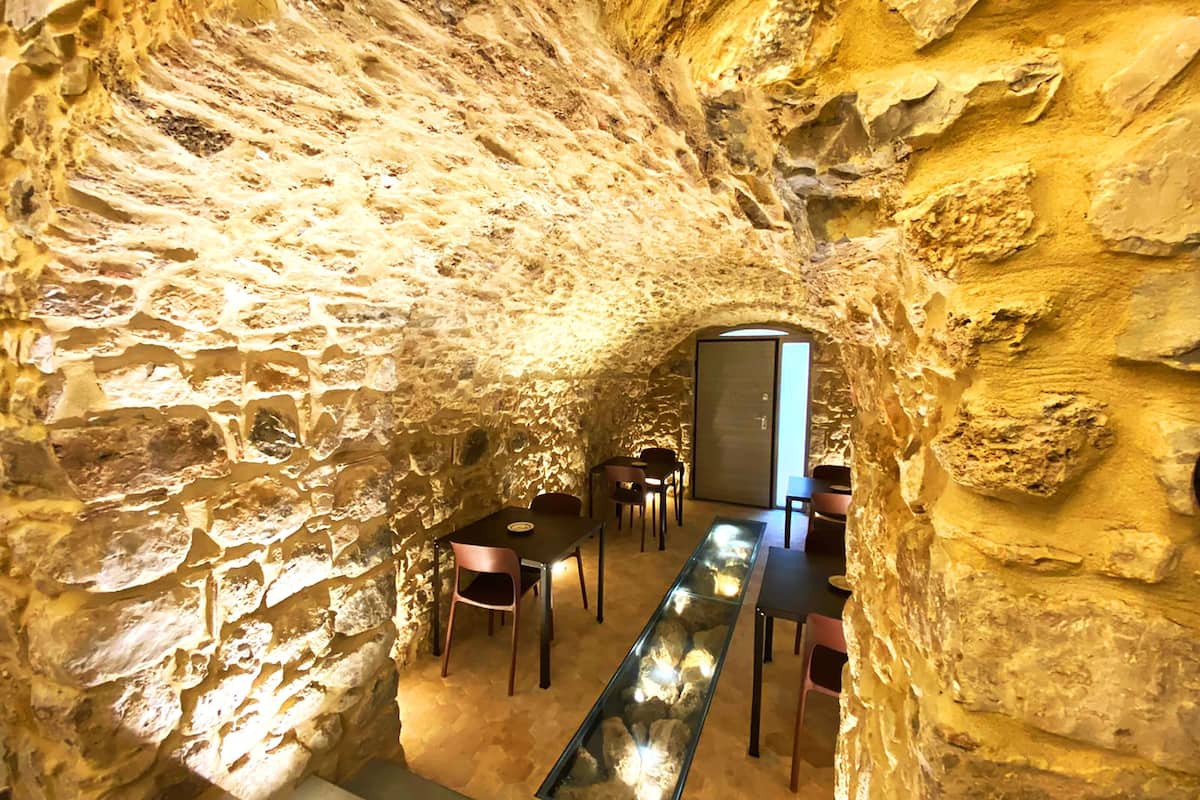 A stone-walled interior with a long table and chairs, a glass display case, and a door leading to another room.