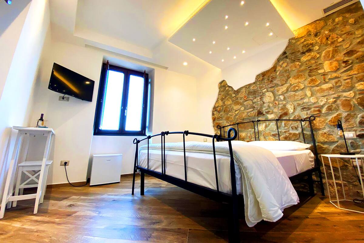 A bedroom with a stone wall, a bed, a TV, and a window.