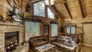 Ein gemütliches Blockhaus-Interieur mit Kamin aus Stein, zwei Sofas, einem Couchtisch und einem Essbereich.