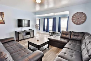 A living room with a sofa set, a coffee table, a TV, and a clock on the wall.