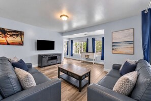 A living room with a flat-screen TV, leather sofas, a coffee table, and artwork on the walls. - Shortstop Apt 2 - All Star Baseball Rentals (Oneonta)