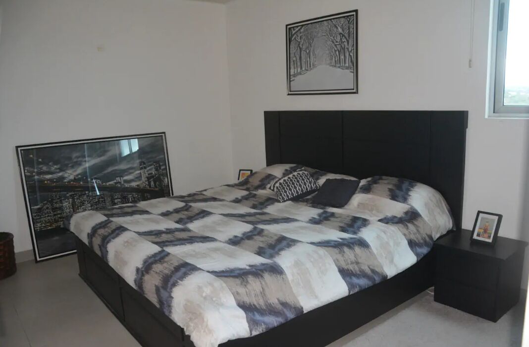 A bedroom with a large bed, a cityscape artwork on the wall, and a framed picture on the nightstand.