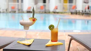 Deux cocktails sur une table près d’une piscine, avec des chaises longues et des parasols en arrière-plan.