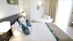 Une chambre d’hôtel avec un grand lit, une table de chevet, une commode, une lampe fixée au mur et une fenêtre avec des rideaux.