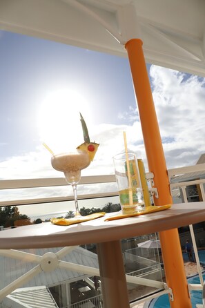 A balcony with a drink and a glass of water, a pool in the background, and a clear sky. - Hotel Saint - Georges (Saint-Claude)