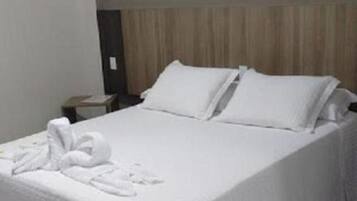 Quarto de hotel com cama bem arrumada, mesa de cabeceira, obra de arte na parede e chão de azulejos.
