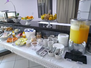 A buffet setup with various food items, including fruits, vegetables, and condiments, arranged on a table with a white lace border.