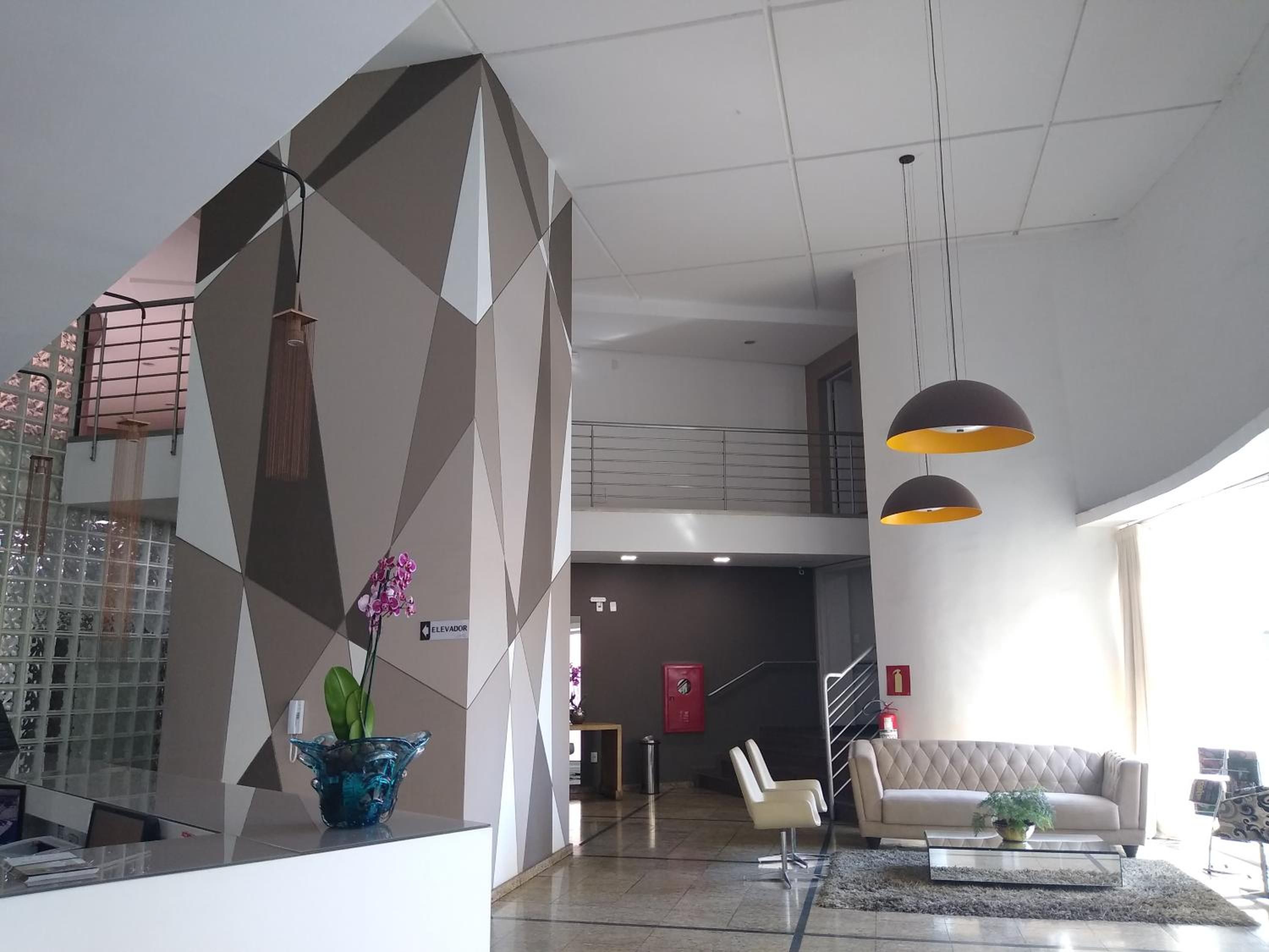 Un hall d’entrée moderne avec un mur au motif géométrique, un comptoir d’accueil, un escalier et un espace détente comprenant un canapé et des fauteuils.