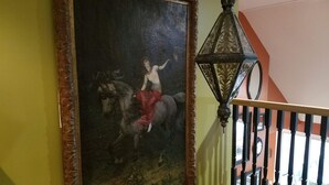 Una escalera con barandilla, un cuadro de una mujer a caballo colgado en la pared y un farol decorativo.