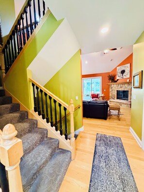 Un escalier avec une rampe en bois et des balustres noires, menant à un espace de vie comprenant une cheminée, un canapé et une table basse.