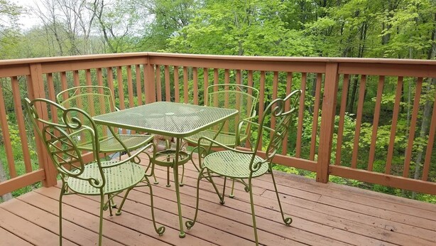 Una terraza de madera con una mesa y sillas de metal, rodeada por una barandilla de madera.
