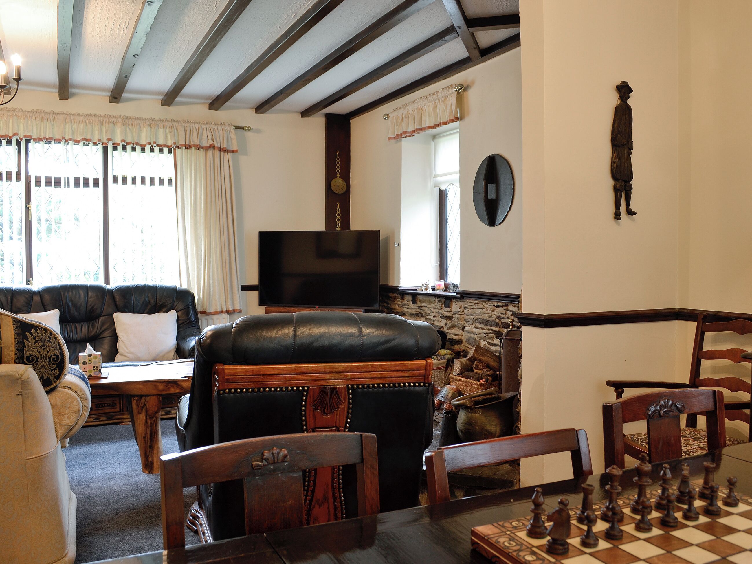 Ein Wohnzimmer mit Ledersofa, einem Holzesstisch mit Schachspiel, einem Fernseher und einem Steinkamin.