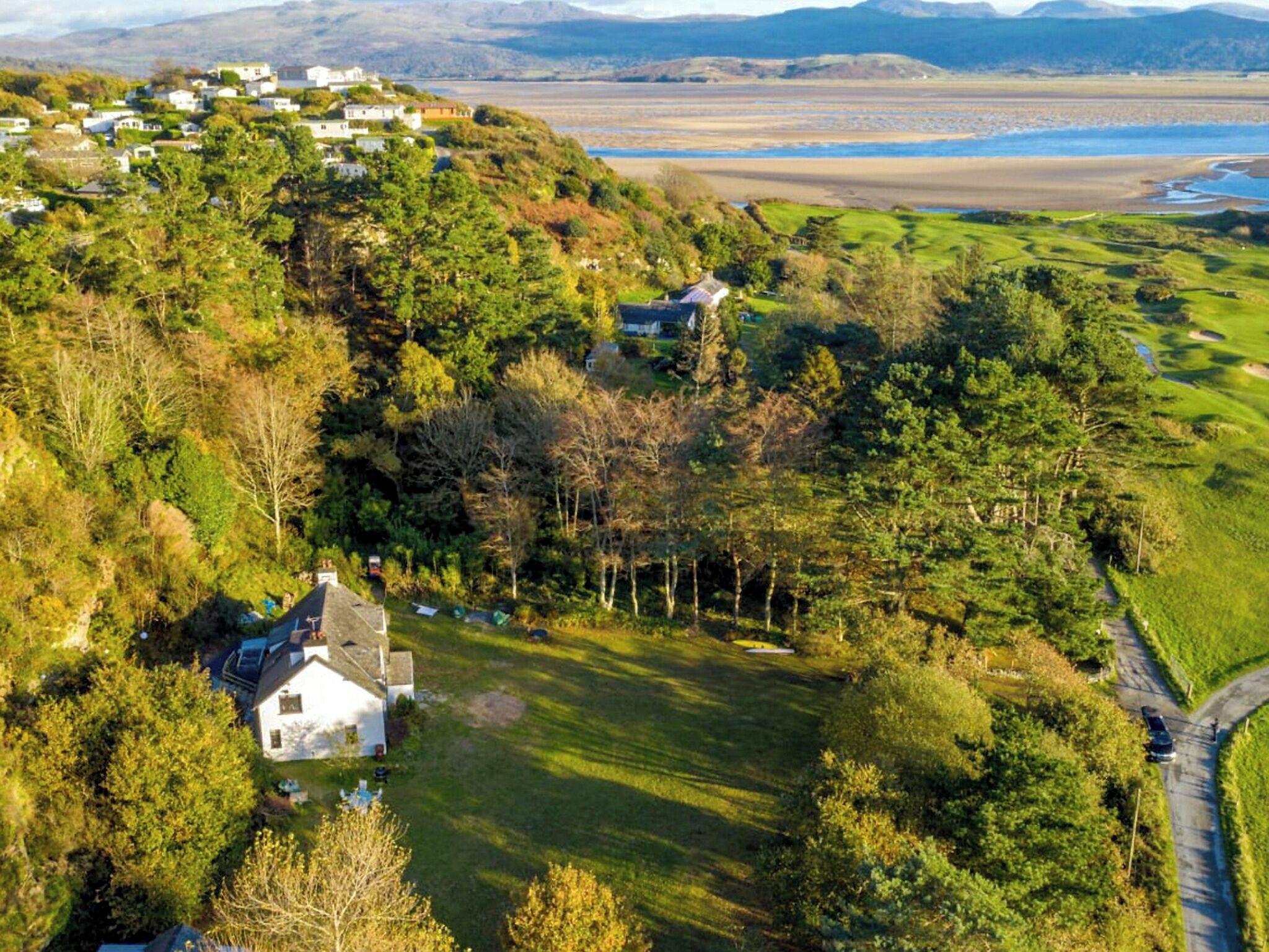 A coastal village with houses on a hillside, a golf course, and a beach in the background.