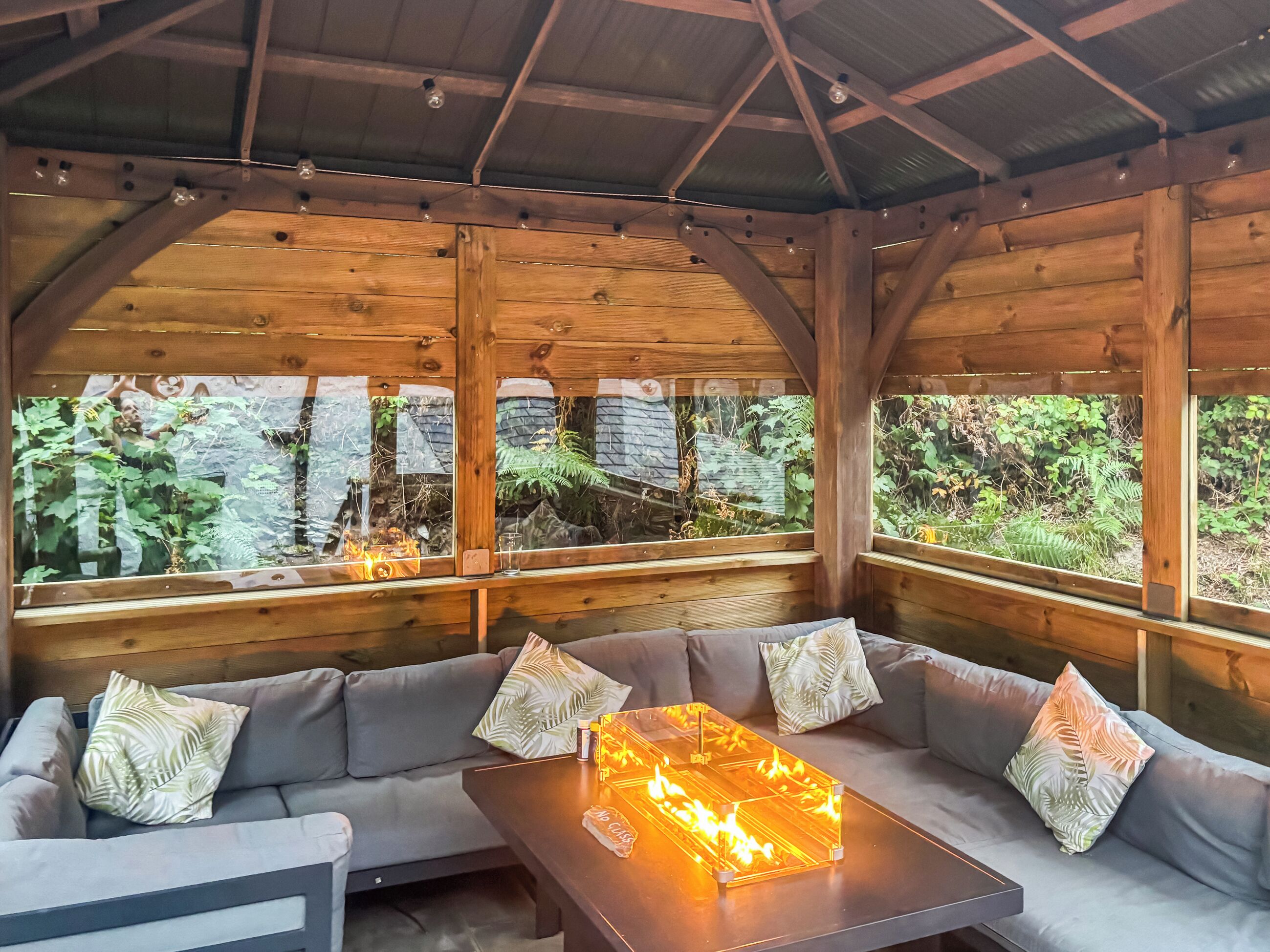 A wooden interior with a sofa and a glass-top table with a fire feature.