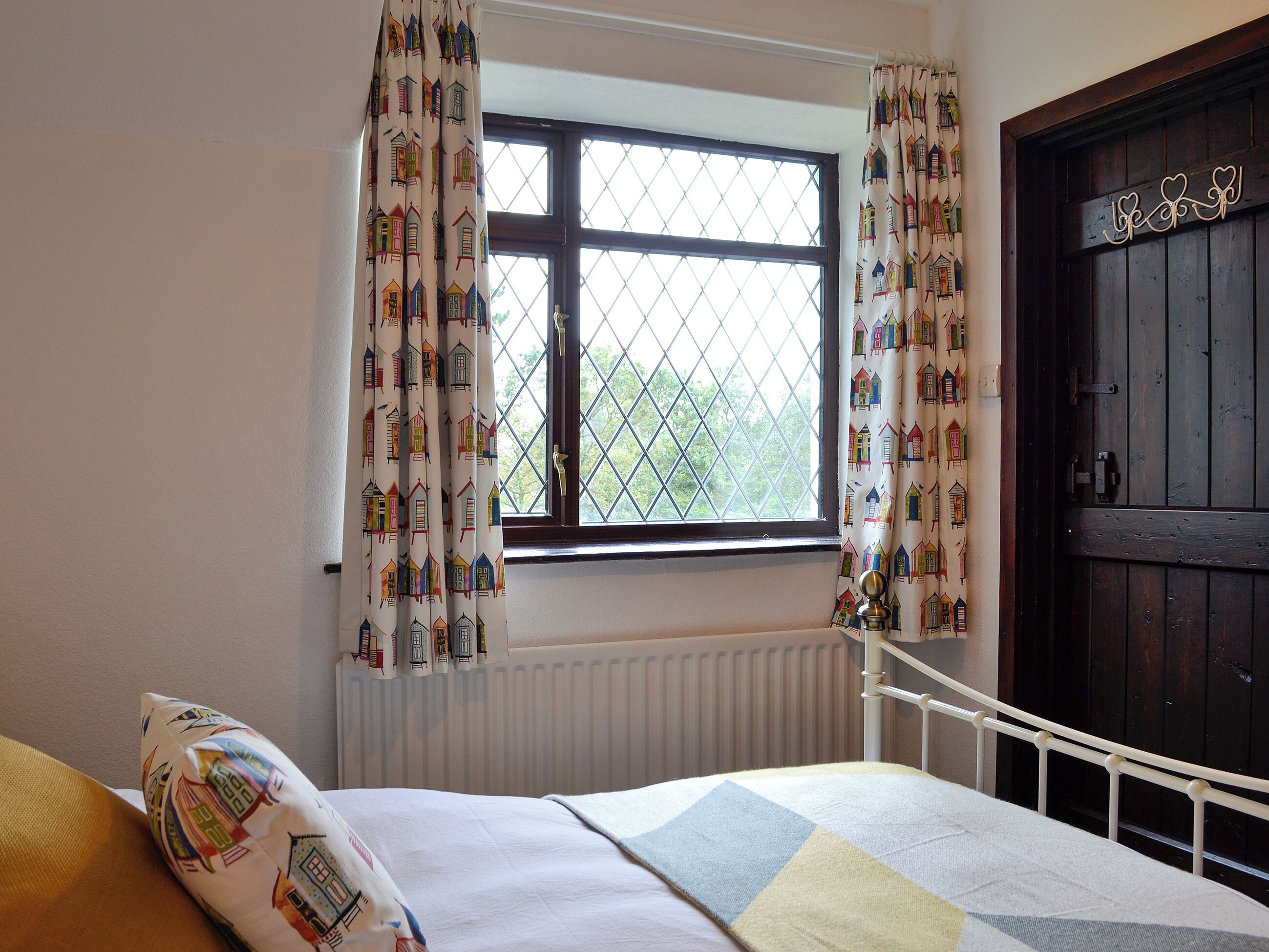 Quarto com cama, janela com cortinas, radiador e porta de madeira.