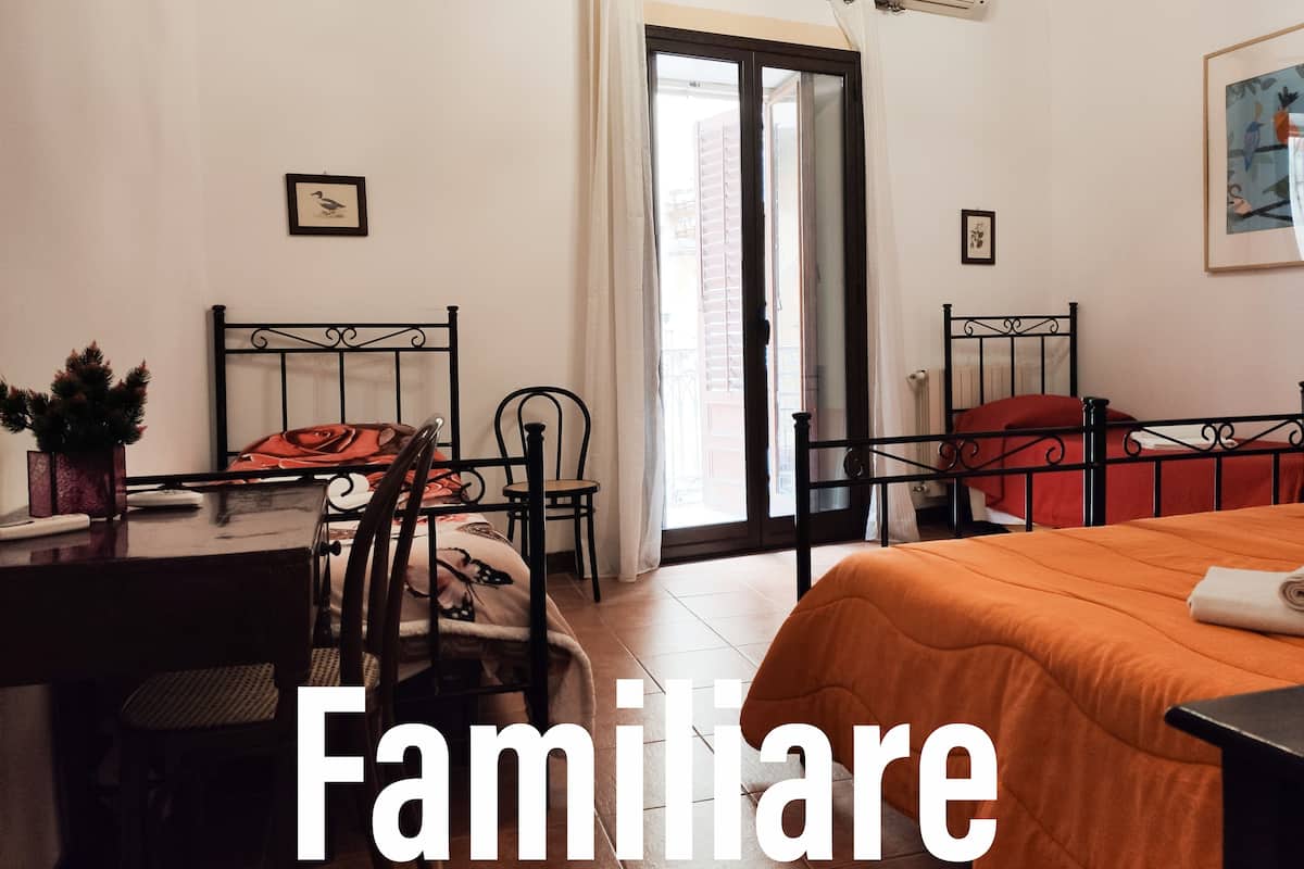 Un dormitorio con cama, escritorio y silla. Se observa una ventana con cortinas y un radiador en la pared.