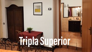 Una habitación con una mesa de comedor, sillas, una planta en maceta, un cuadro enmarco y una puerta que da a un baño con lavamanos y espejo.