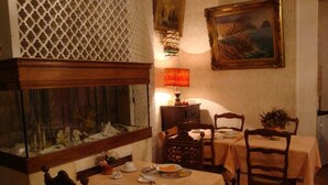 A dining area with two tables set for two, wooden chairs, a fish tank, and a painting on the wall. - Hotel Cronstadt (Nice)