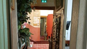 A hallway with a red patterned carpet, a large potted plant, and a metal gate. - Hotel Cronstadt (Nice)