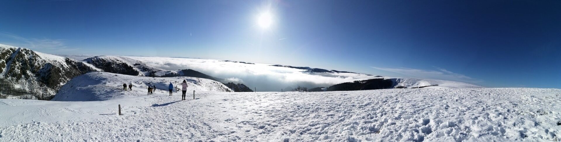 Paesaggio montano innevato con cieli sereni e alcune persone che camminano.