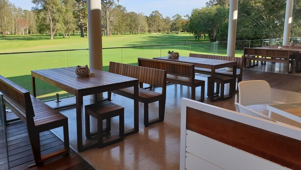 Een terras buiten met houten tafels en banken, met uitzicht op een golfbaan.