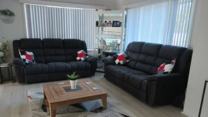 Een woonkamer met twee zwarte banken, een houten salontafel met een plant en een kamerkleed met dessin.