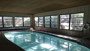 Una piscina interior con paredes de vidrio transparente, un borde azul y una banca a lo largo de la pared.