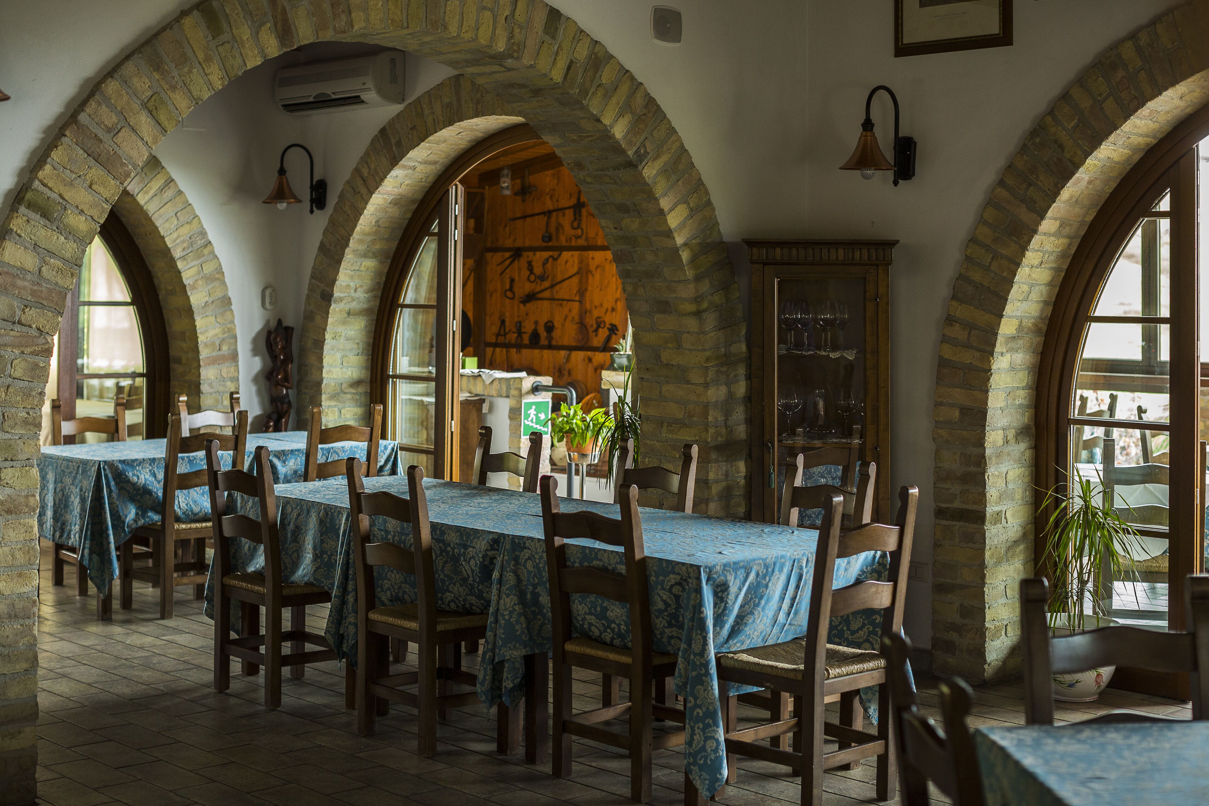 Un espace repas avec une longue table recouverte d’une nappe bleue, entourée de chaises en bois.