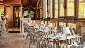 Un restaurante con terraza, mesas dispuestas con copas de vino y platos, y vistas al exterior.