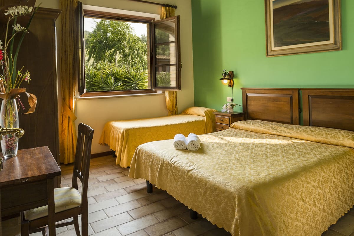 Ein Zimmer mit einem Bett, einem Schreibtisch und einem Fenster mit Blick auf Grünflächen.
