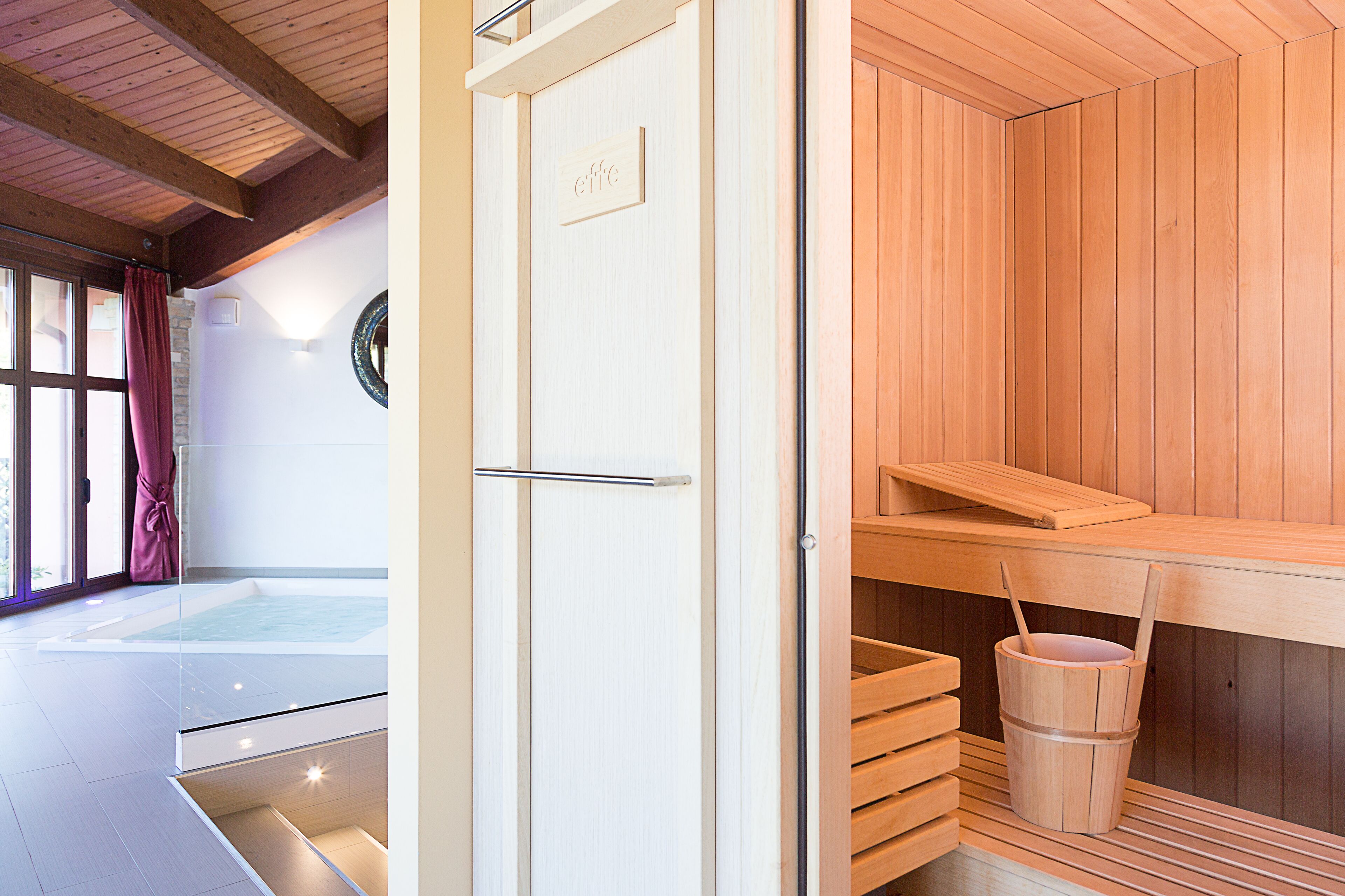 Ein moderner Wellnessraum mit einem gläsernen Whirlpool, Holz-Saunabänken und einem Holzeimer.