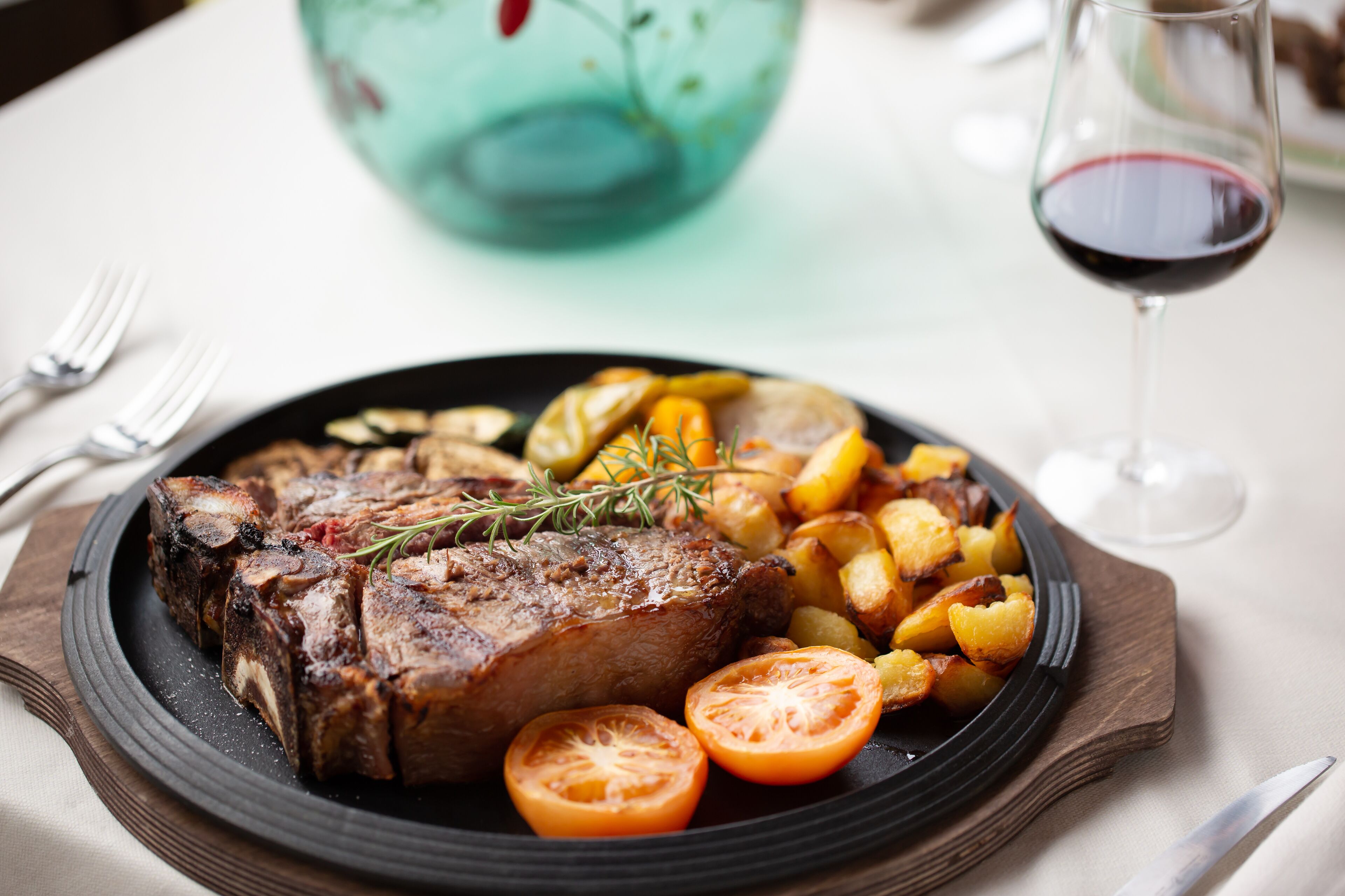 Ein Teller mit Steak, gerösteten Kartoffeln und Tomaten, dazu ein Glas Rotwein.