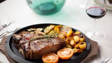 Ein Teller mit Steak, gerösteten Kartoffeln und Tomaten, dazu ein Glas Rotwein.