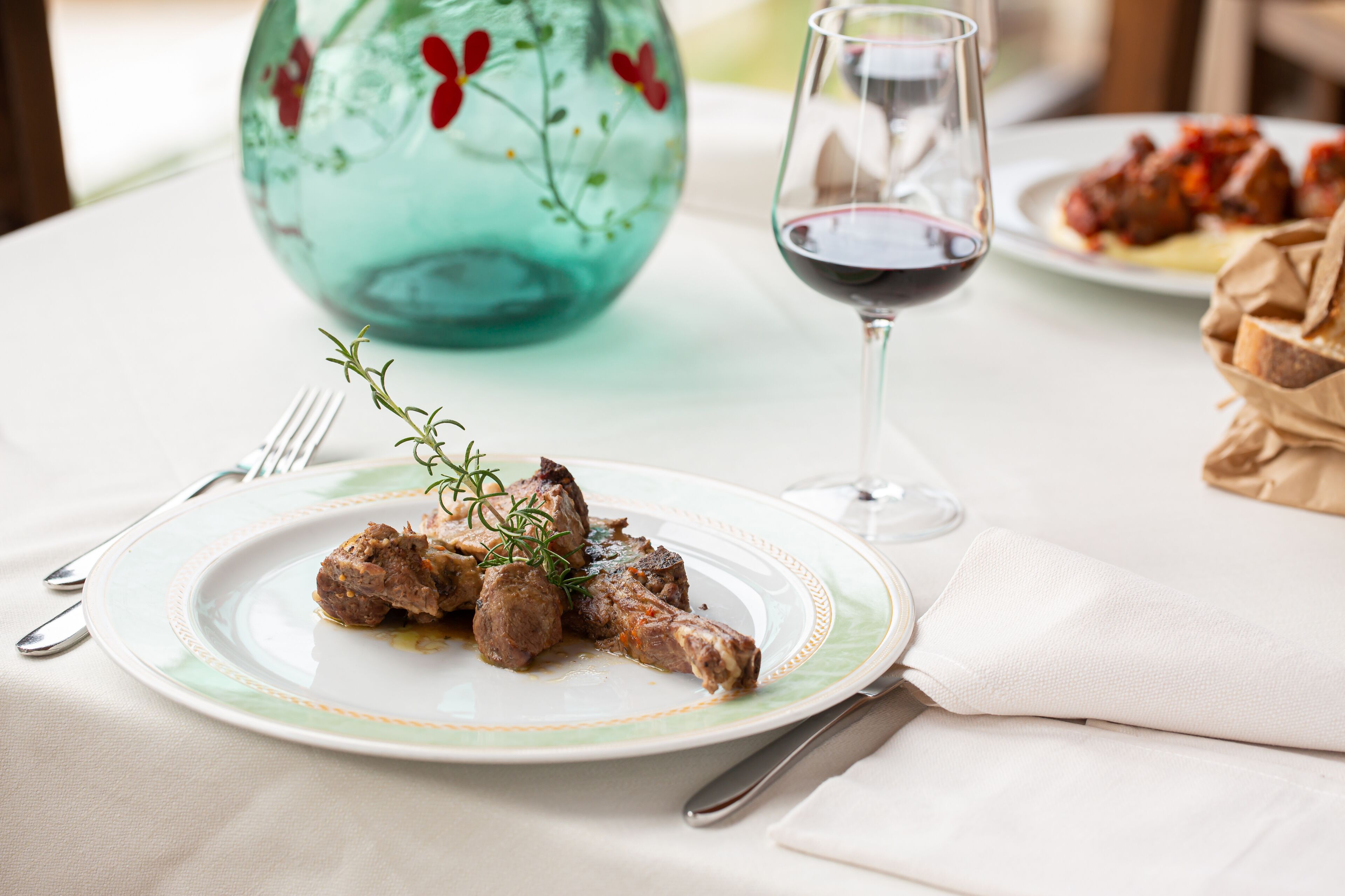 Une assiette de nourriture, un verre de vin rouge et un vase décoratif posés sur une table.