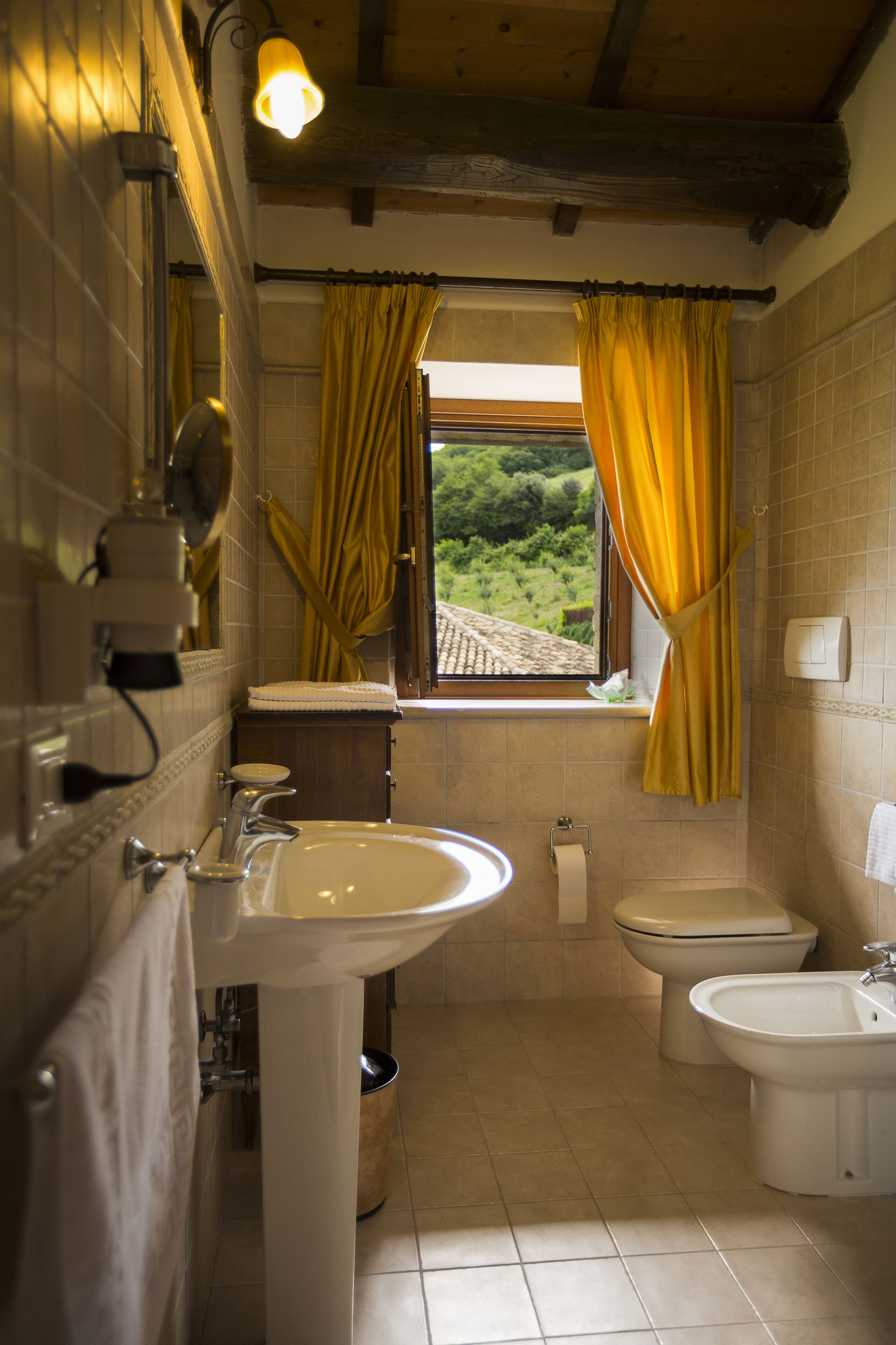 A bathroom with a sink, toilet, bidet, and a window with curtains.