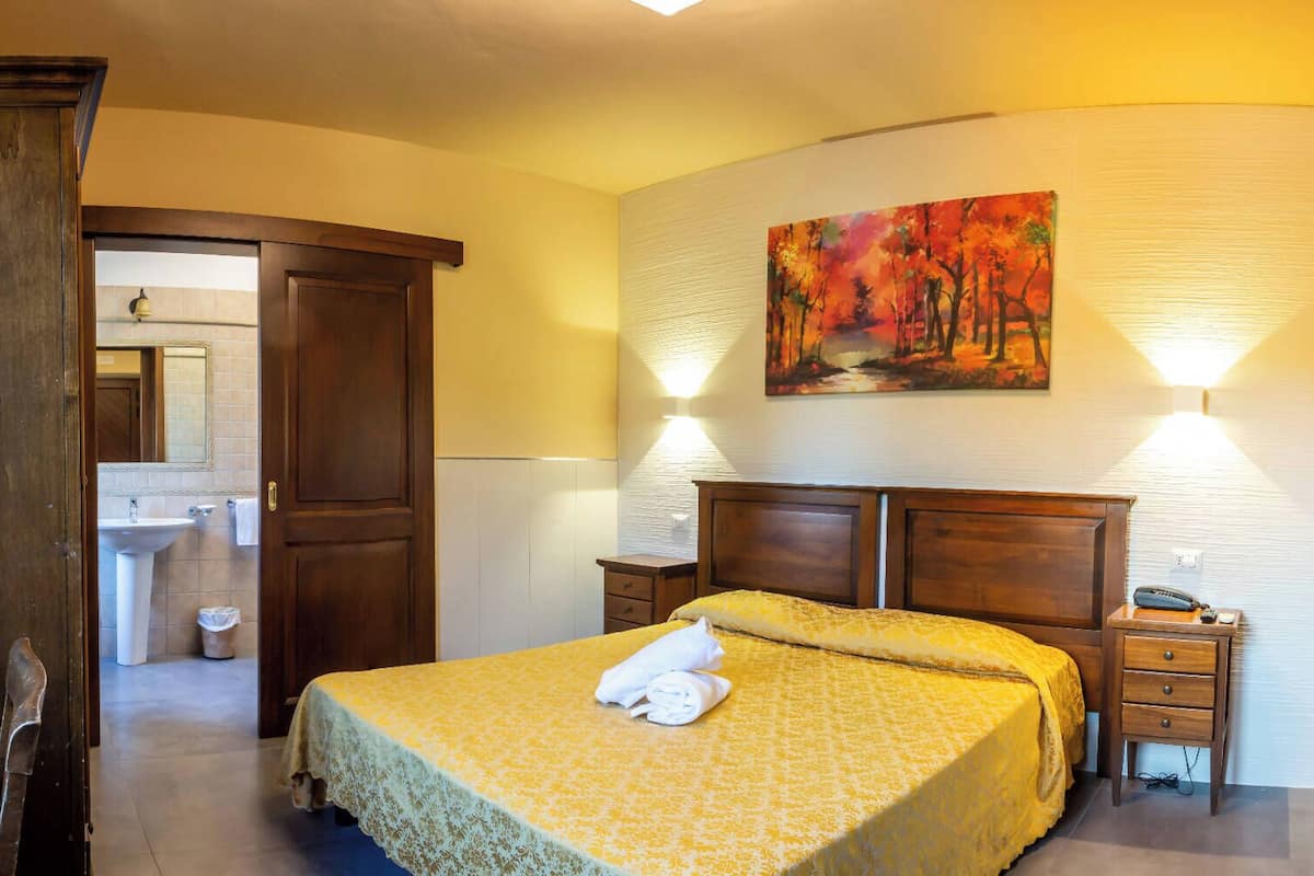 Ein Schlafzimmer mit einem Bett, einem Nachttisch, einem Bild, einer Tür und einem durch eine offene Tür einsehbaren Badezimmer.