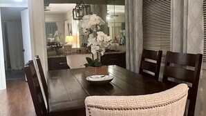 Ein Esszimmer mit einem dunklen Holztisch, weißen Stühlen mit Muster und einer Vase mit weißen Blumen.