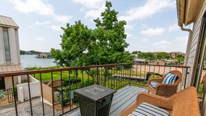 Ein Balkon mit Korbmöbeln, einem kleinen Tisch und Blick auf einen See sowie entfernte Gebäude.